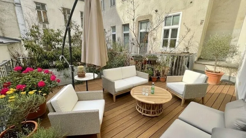 Möblierte Terrasse mit Holzdeck, Sonnenschirm und Pflanzen in einem Innenhof.