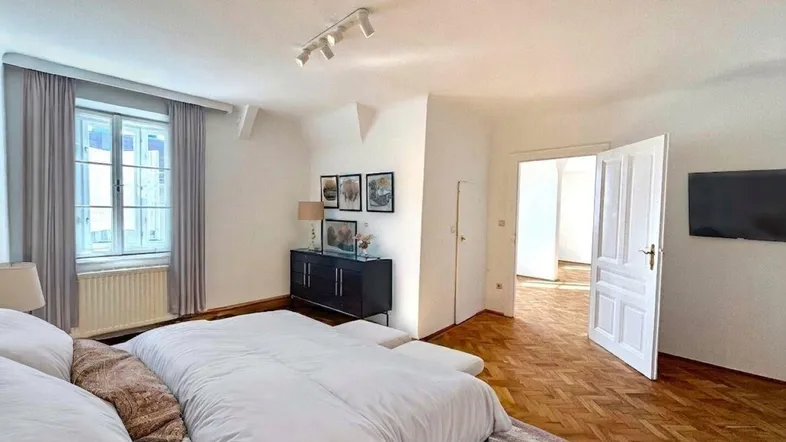 Helles Schlafzimmer mit Parkettboden, großem Bett und Blick aus dem Fenster.