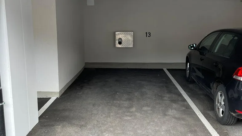 Geräumiger Tiefgaragenstellplatz Nummer 13 mit einem geparkten Auto und einer Ladestation an der Wand.
