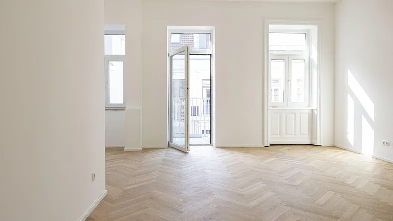 Helles Zimmer mit Fischgrätparkett und Zugang zu einem französischen Balkon.