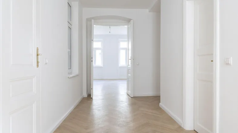 Heller Flur mit Fischgrätparkett und weißen Türen, der zu einem weiteren lichtdurchfluteten Raum führt.