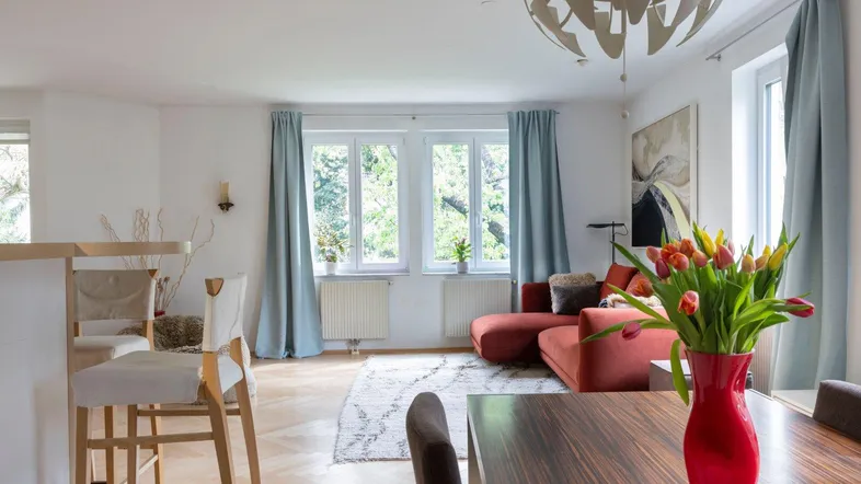Helles Wohn- und Esszimmer mit Parkettboden, rotem Sofa und Blick ins Grüne.