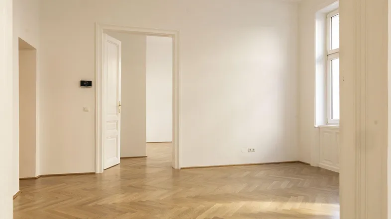Helles Zimmer mit Fischgrätparkett und hohen weißen Wänden, bereit zur individuellen Gestaltung.