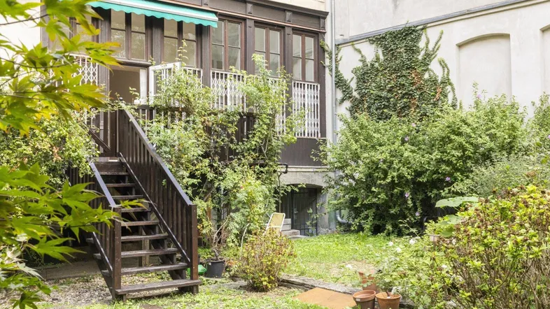 Grüner Hinterhofgarten mit Treppe, die zu einem Balkon oder einer Terrasse führt, umgeben von üppiger Vegetation.