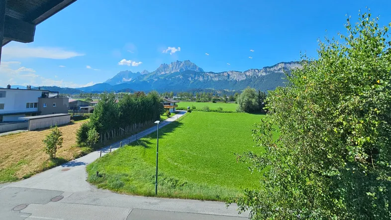 Panoramablick vom Balkon auf grüne Felder und die majestätische Berglandschaft unter blauem Himmel.
