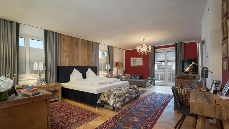 Geräumiges Schlafzimmer mit Holzakzenten, roter Wand und integriertem Wohn- und Arbeitsbereich.