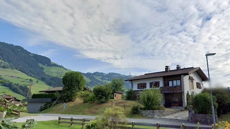 Haus in alpiner Landschaft mit grünen Hügeln und bewölktem Himmel, umgeben von Natur.