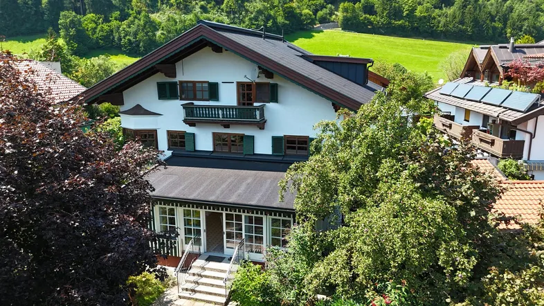 Traditionelles Haus im alpenländischen Stil mit grünen Fensterläden und umgeben von viel Grün.