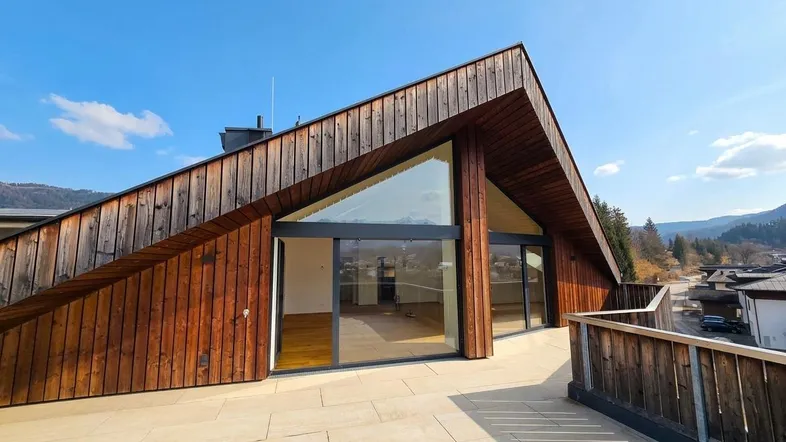 Moderne Dachgeschosswohnung mit Holzfassade, großer Terrasse und weitem Blick auf die Umgebung.