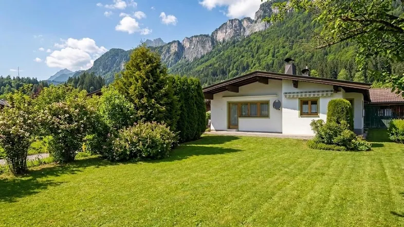 Gepflegter Garten mit Rasenfläche und Sträuchern vor einem Haus mit Bergblick.