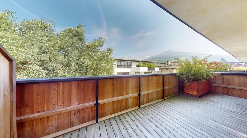 Geräumige Terrasse mit Holzboden, Pflanzenkübeln und Bergblick unter blauem Himmel.