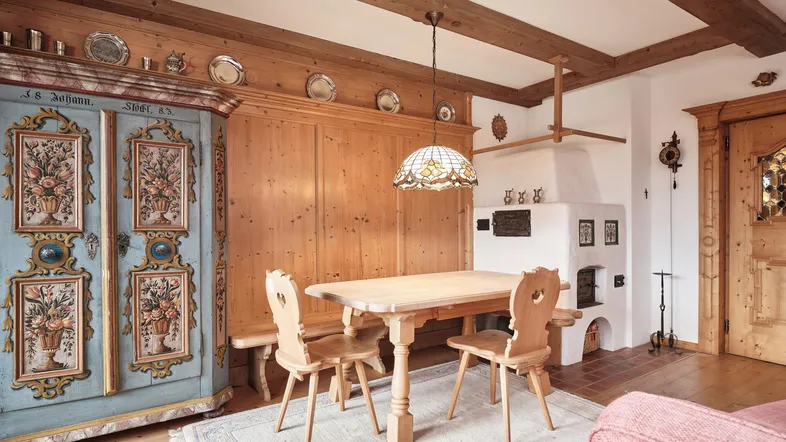 Gemütlicher Essbereich im alpinen Stil mit Holzbalken, Kachelofen und handbemaltem Schrank.