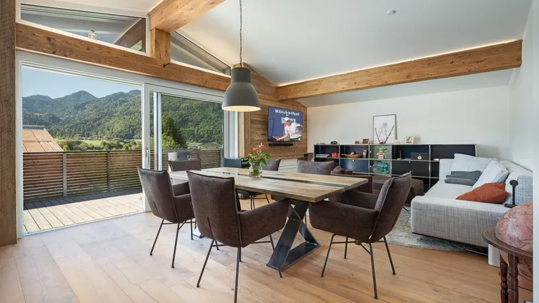 Heller Wohn- und Essbereich mit Holzbalken, Parkettboden und Zugang zu einem Balkon mit Bergblick.