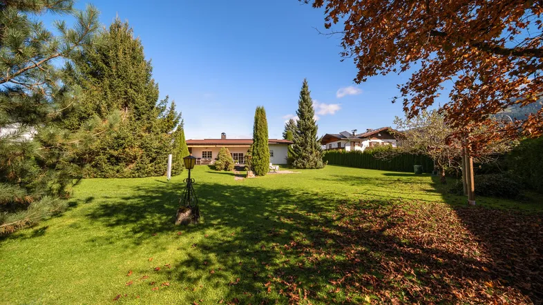 Großer, gepflegter Garten mit Rasenfläche, hohen Bäumen und Blick auf das charmante Einfamilienhaus.