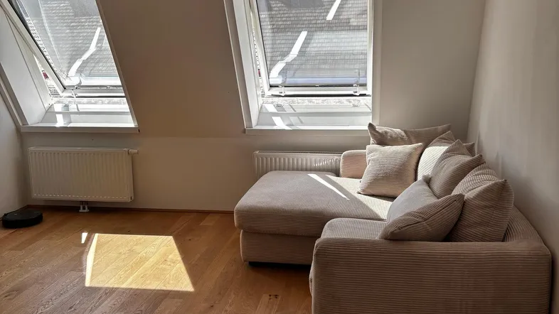 Helles Wohnzimmer im Dachgeschoss mit gemütlichem Sofa, Holzboden und Dachfenstern.