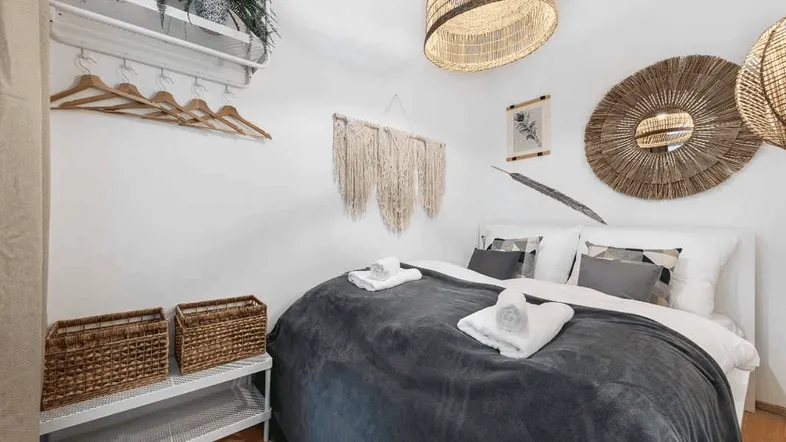 Helles Schlafzimmer mit Doppelbett, Holzboden und dekorativen Wandelementen im Boho-Stil.