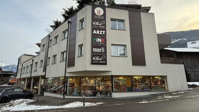Modernes Geschäftsgebäude mit mehreren Etagen und großen Schaufenstern, umgeben von Schnee und Bergen.