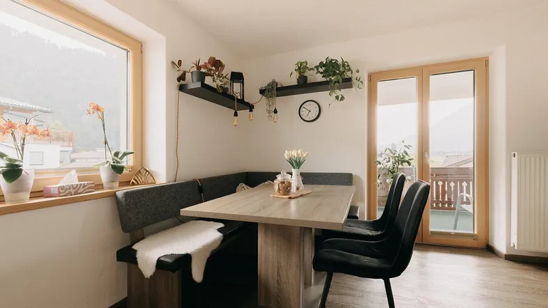 Heller Essbereich mit Eckbank, Holztisch und Zugang zum Balkon, umgeben von Pflanzen.