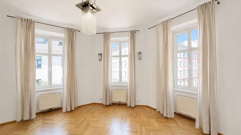 Geräumiges Zimmer mit Fischgrätparkett, hohen Fenstern und einem Blick auf die umliegenden Gebäude.