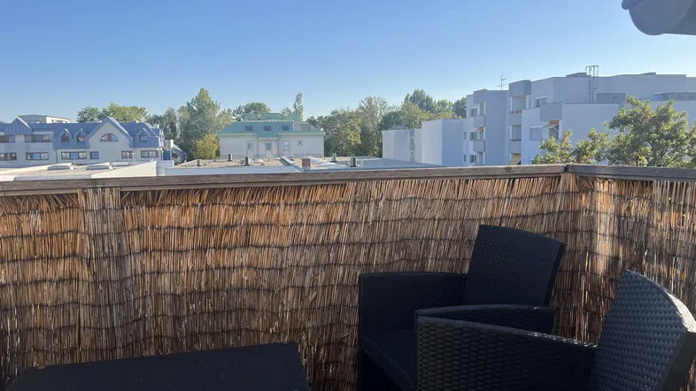 Gemütliche Terrasse mit Korbmöbeln und Blick auf die umliegenden Gebäude unter blauem Himmel.