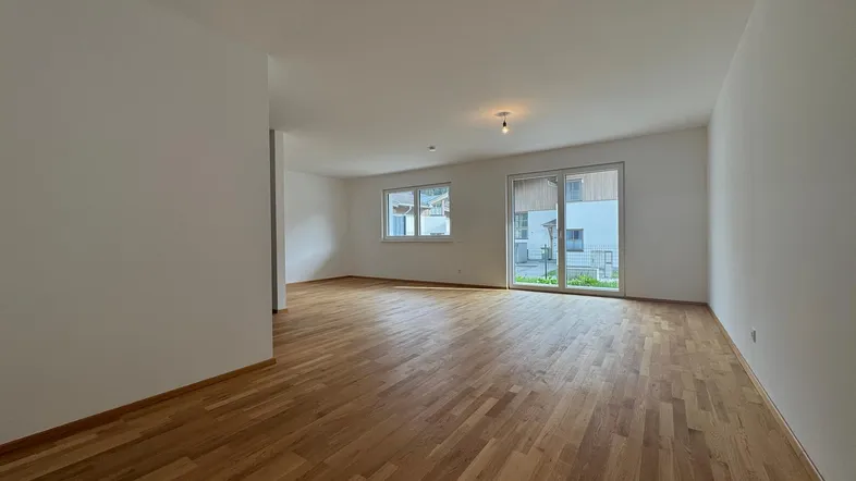 Helles, leeres Zimmer mit Holzboden und Zugang zu einem Außenbereich, ideal als Wohnzimmer.