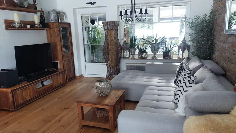 Gemütliches Wohnzimmer mit großem Sofa, Holzboden und dekorativer Steinwand, hell durch große Fenster.