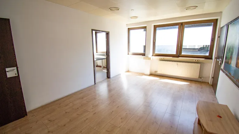 Heller, leerer Raum mit Laminatboden und großen Fenstern, der sich als Büro oder Wohnbereich eignet.