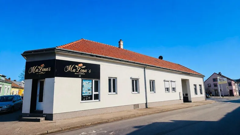 Außenansicht eines Geschäftsgebäudes mit weißer Fassade und rotem Ziegeldach an einem sonnigen Tag.