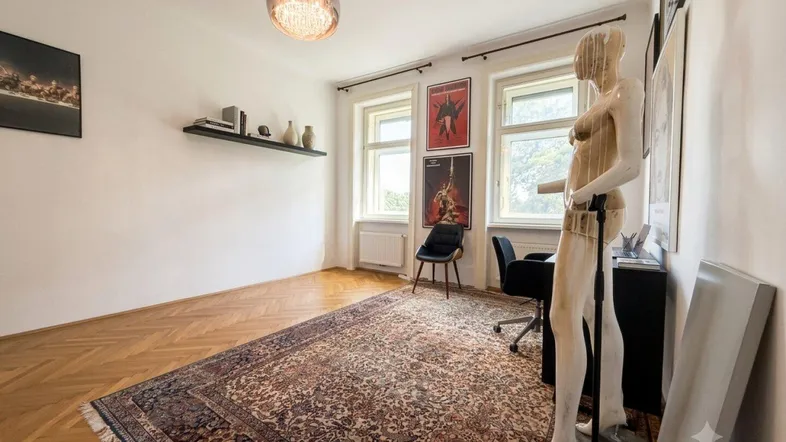 Helles Zimmer mit Fischgrätparkett, großem Teppich und Arbeitsbereich am Fenster.