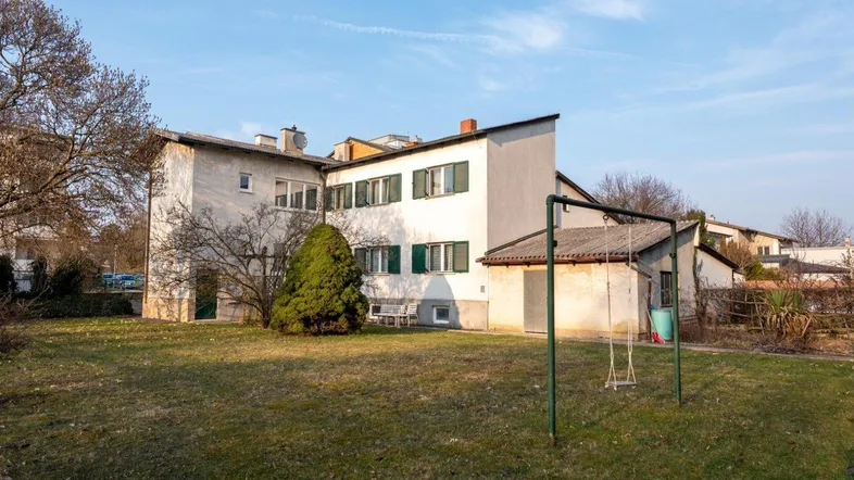 Großer Garten hinter dem Haus mit Rasenfläche und Schaukel, umgeben von Bäumen und Sträuchern.