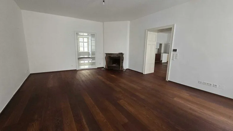 Geräumiger Wohnbereich mit dunklem Parkettboden und einem historischen Kamin.