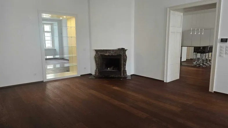 Geräumiges Wohnzimmer mit dunklem Parkettboden und einem dekorativen Kamin als Blickfang.