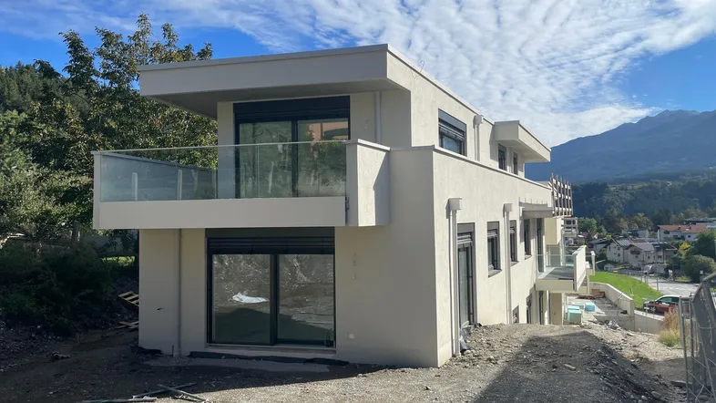 Modernes Mehrfamilienhaus im Bau mit Balkonen und Blick auf die Berge.