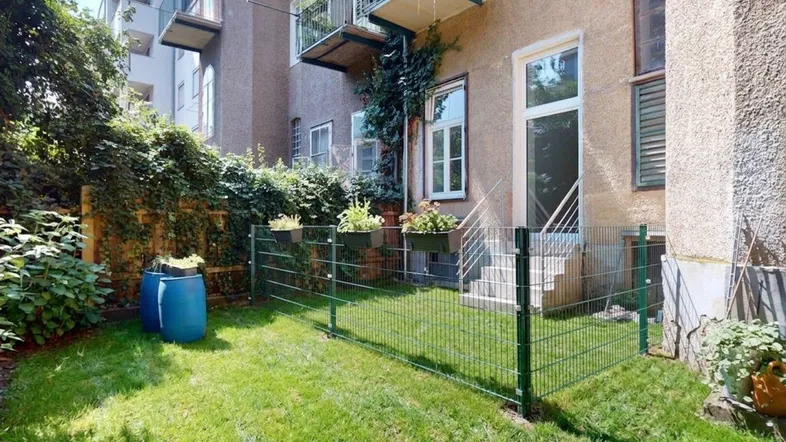 Kleiner, eingezäunter Gartenbereich mit Rasenfläche und Zugang zum Gebäude, umgeben von üppigem Grün.