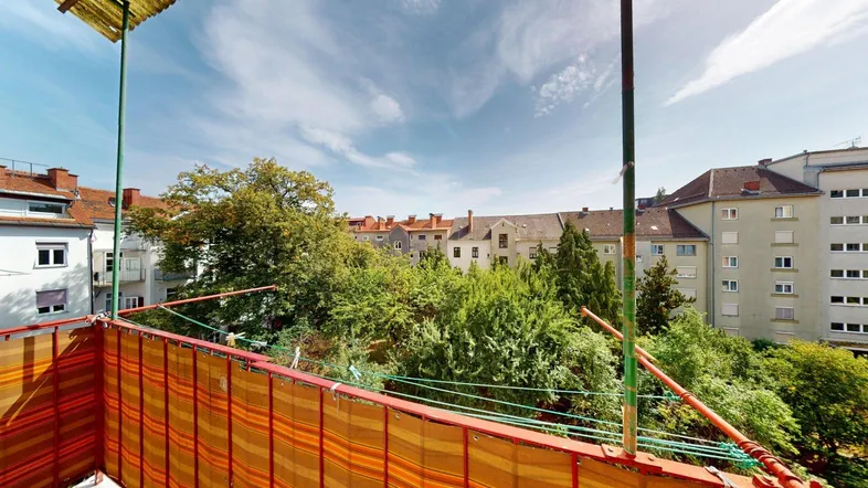 Blick vom Balkon mit gestreiftem Sichtschutz und grüner Umgebung, umgeben von Wohngebäuden.