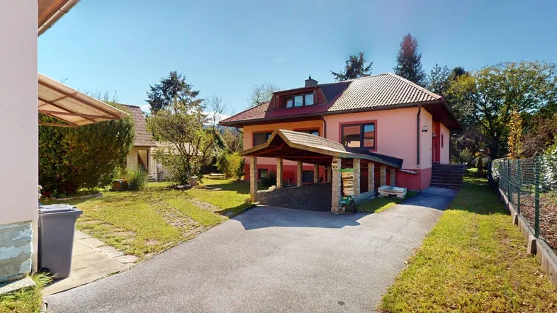 Einfamilienhaus mit Carport und gepflegtem Vorgarten unter blauem Himmel.