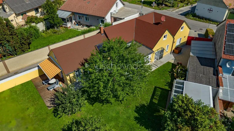 Luftaufnahme eines gelben Einfamilienhauses mit großem Garten, Terrasse und umliegender Wohnsiedlung.