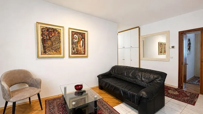 Helles Wohnzimmer mit schwarzem Ledersofa, modernem Glastisch und Parkettboden.