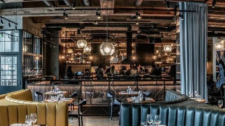 Geräumiger Restaurantbereich mit Holzbalkendecke, gemütlichen Sitzgelegenheiten und einer beleuchteten Bar im Hintergrund.