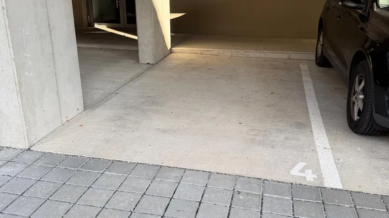 Überdachter Parkplatz im Erdgeschoss eines Wohngebäudes mit Briefkästen an der Wand und natürlichem Lichteinfall.