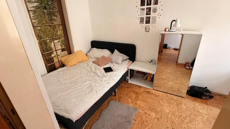 Gemütliches Schlafzimmer mit Einzelbett, Korkboden und großem Fenster mit Blick ins Grüne.