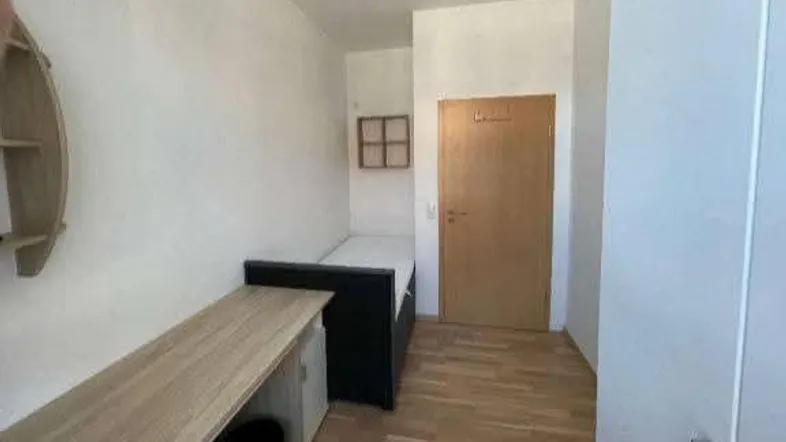 Helles Schlafzimmer mit Holzboden, einem Bett und einem funktionalen Schreibtischbereich.
