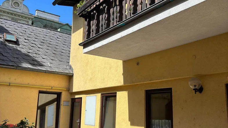 Gemütliche Terrasse mit Sitzgelegenheiten und Zugang zu einem traditionellen Balkon an einem sonnigen Tag.