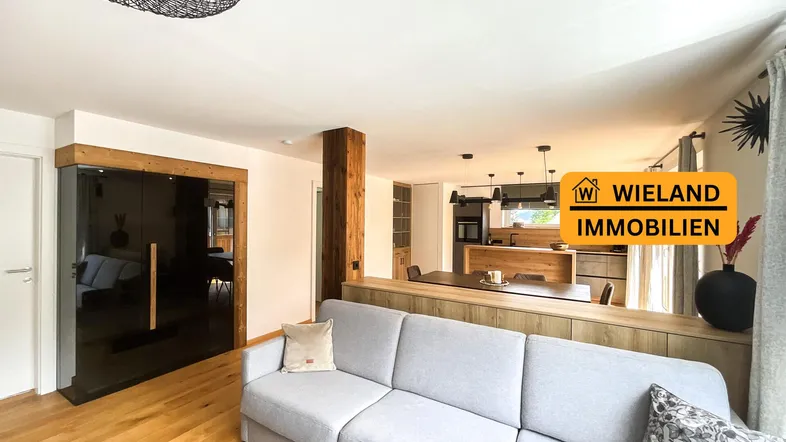 Helles Wohnzimmer mit Holzboden, gemütlichem Sofa und offenem Übergang zur modernen Küche.