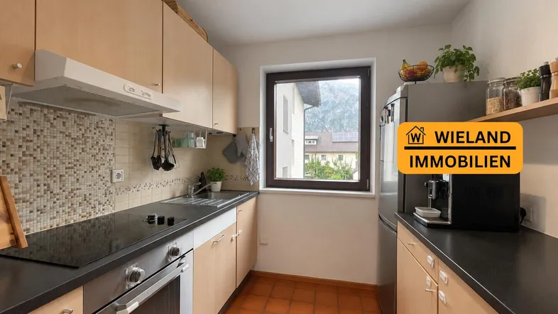 Funktionale Küche mit hellen Holzschränken, dunkler Arbeitsplatte und Fensterblick ins Grüne.