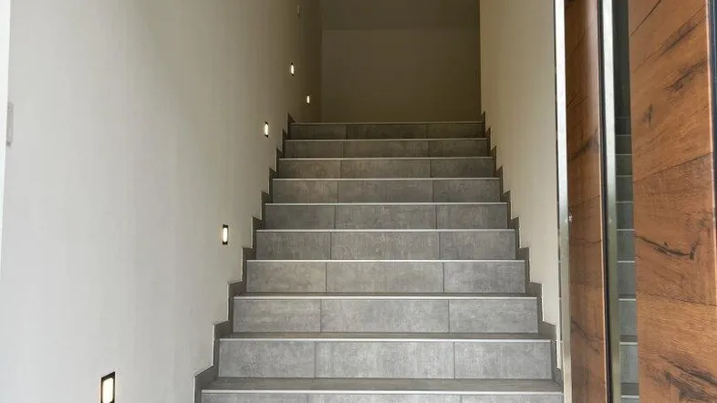 Heller Treppenaufgang mit modernen Fliesenstufen und integrierter Wandbeleuchtung.