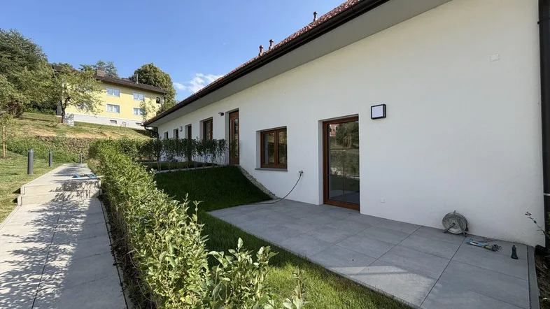 Außenansicht des Gebäudes mit kleiner gepflasterter Terrasse und gepflegter Hecke.