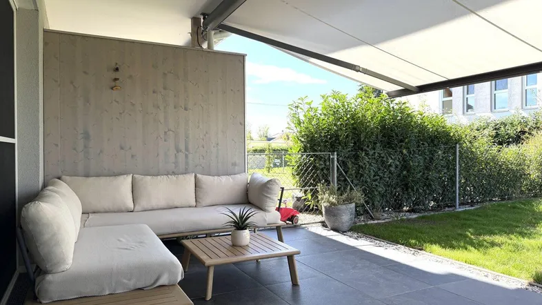 Moderne Terrasse mit bequemen Outdoor-Möbeln und Markise, angrenzend an einen kleinen Gartenbereich.
