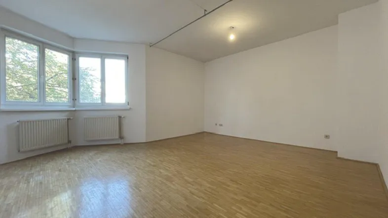 Helles, leeres Zimmer mit Parkettboden und großen Fenstern, bereit zur individuellen Gestaltung.