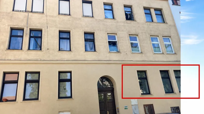 Fassade eines Mehrfamilienhauses mit mehreren Fenstern und einer Eingangstür in städtischer Umgebung.
